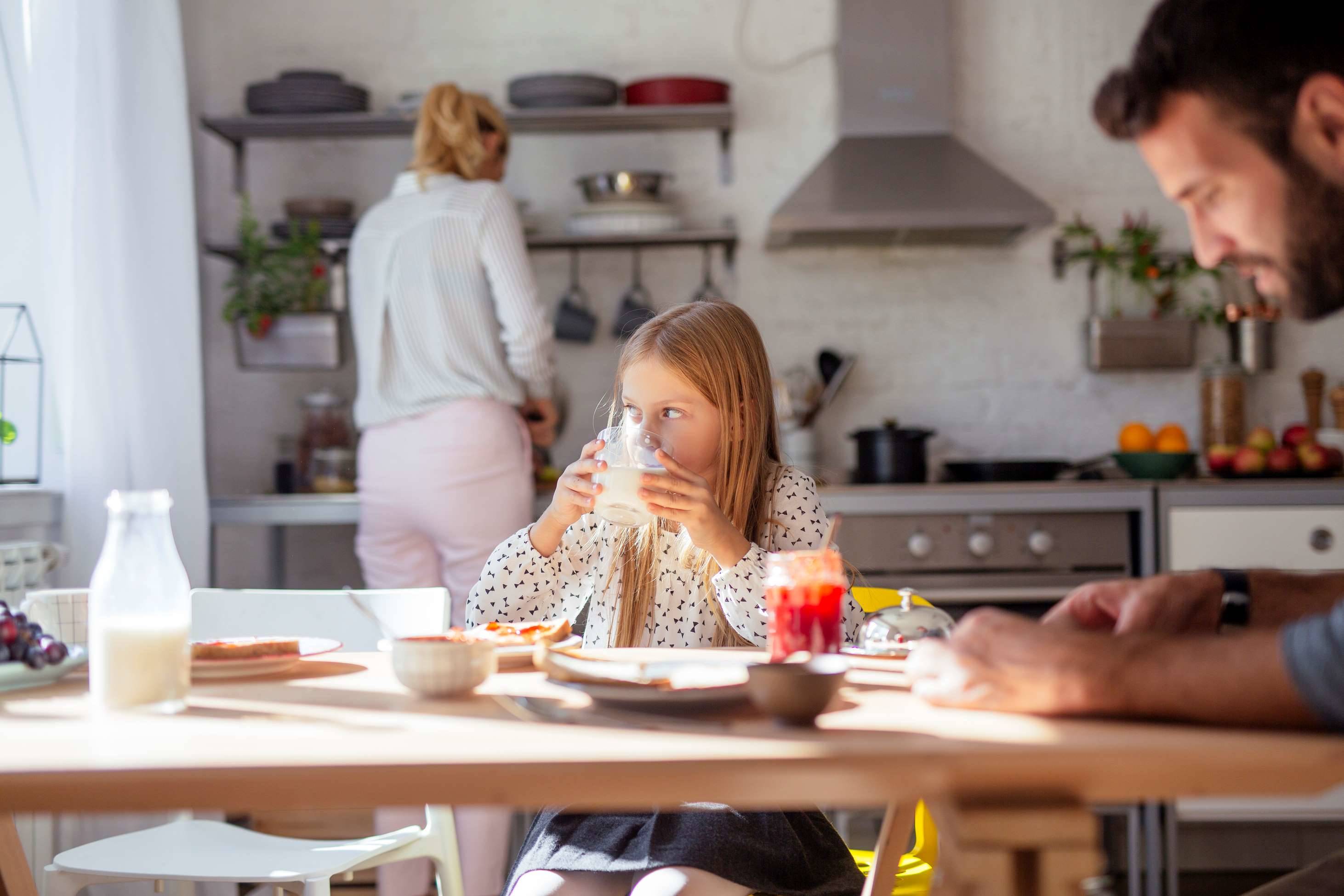 La famille prépare le petit-déjeuner pendant que sa fille apprécie le lait, soulignant le rôle des produits laitiers dans l'alimentation