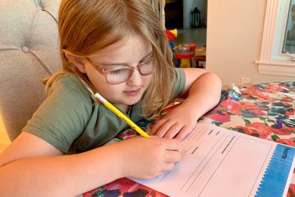 Enfant assise à table qui écrit une recette