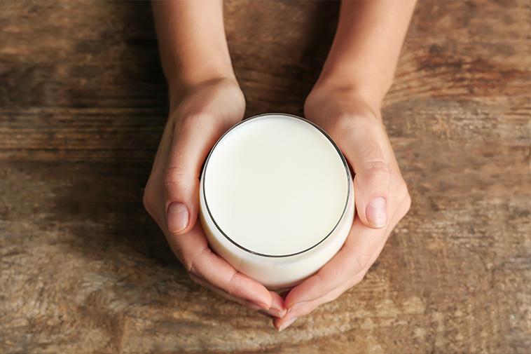 An overhead view of two hands holding a glass full of milk on a wooden table.