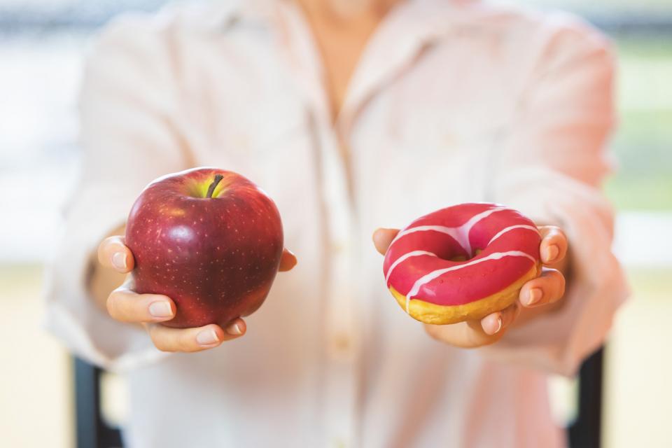 femme qui tient une pomme dans une main et un beigne dans l'autre