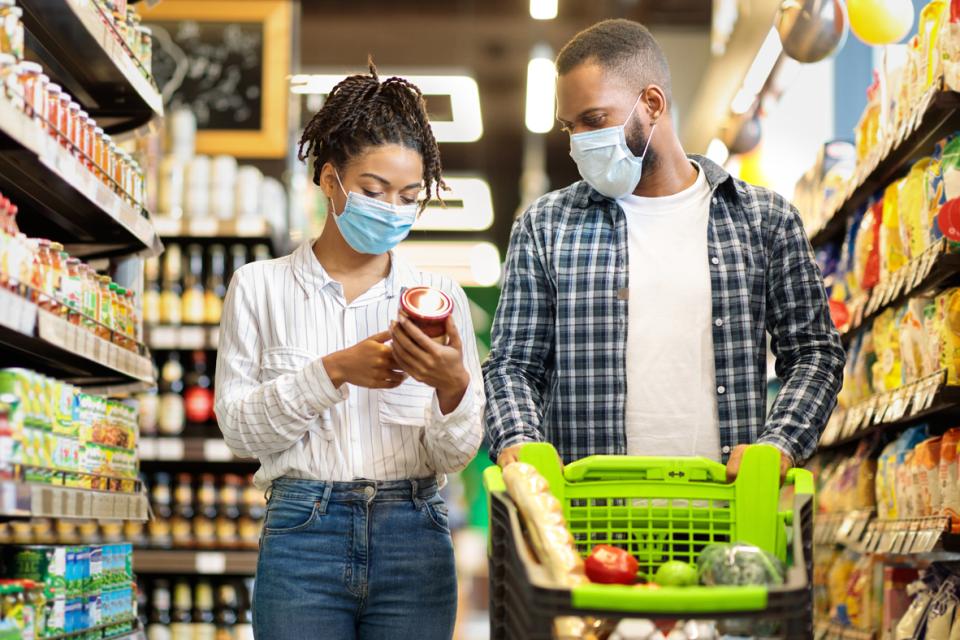 Une femme et un homme portant des masques regardant des étiquettes alimentaires dans une épicerie 