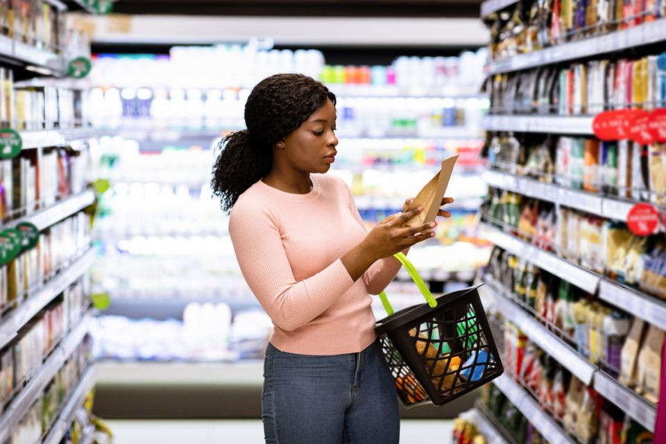 Une femme qui est à l'épicerie et qui regarde des étiquettes nutritionnelles