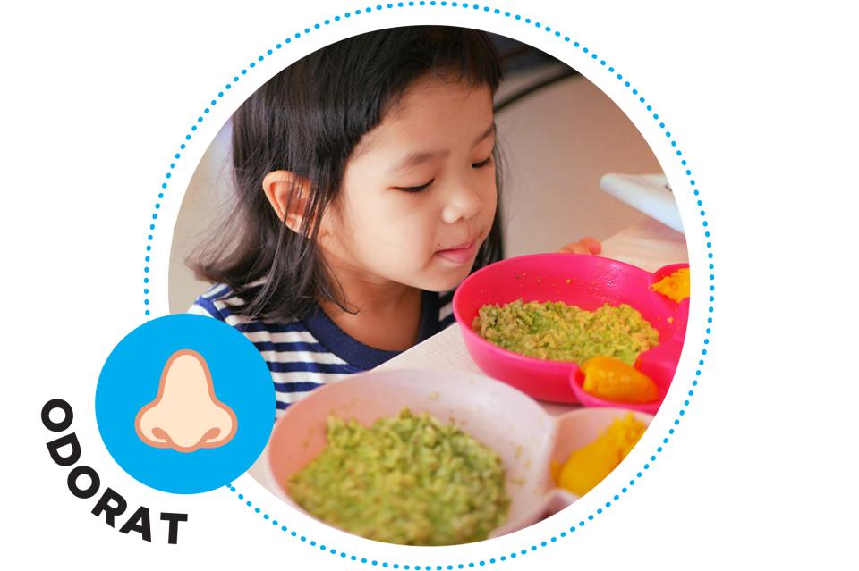 Petite fille sentant des aliments à table.