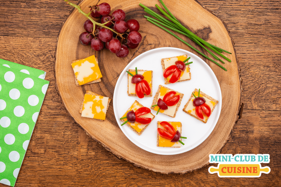 Craquelins carré avec fromage et tomates et raisins tranchés et placés en forme de coccinelle sur un planche en bois