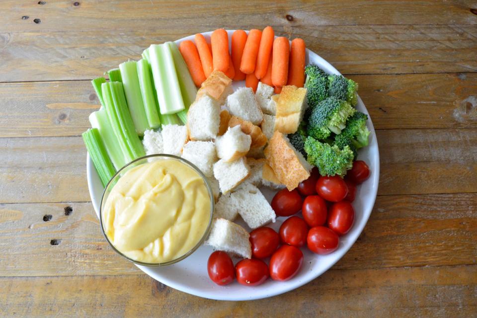 Sauce au fromage dans un bol servi avec du pain et des légumes crus sur une assiette blanche