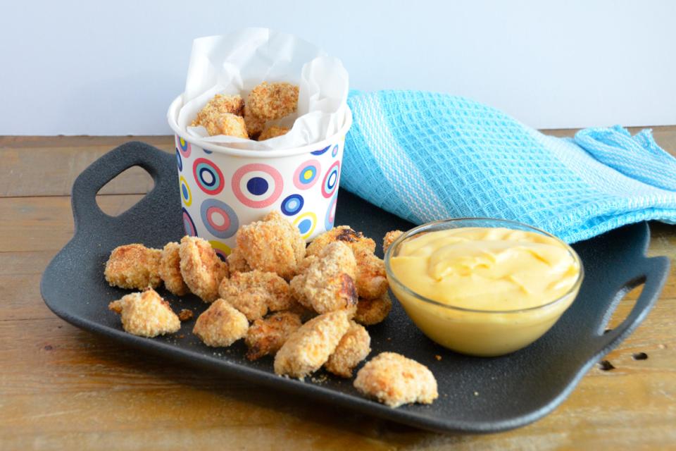 Poulet popcorn servi sur un plateau noir avec une sauce au fromage