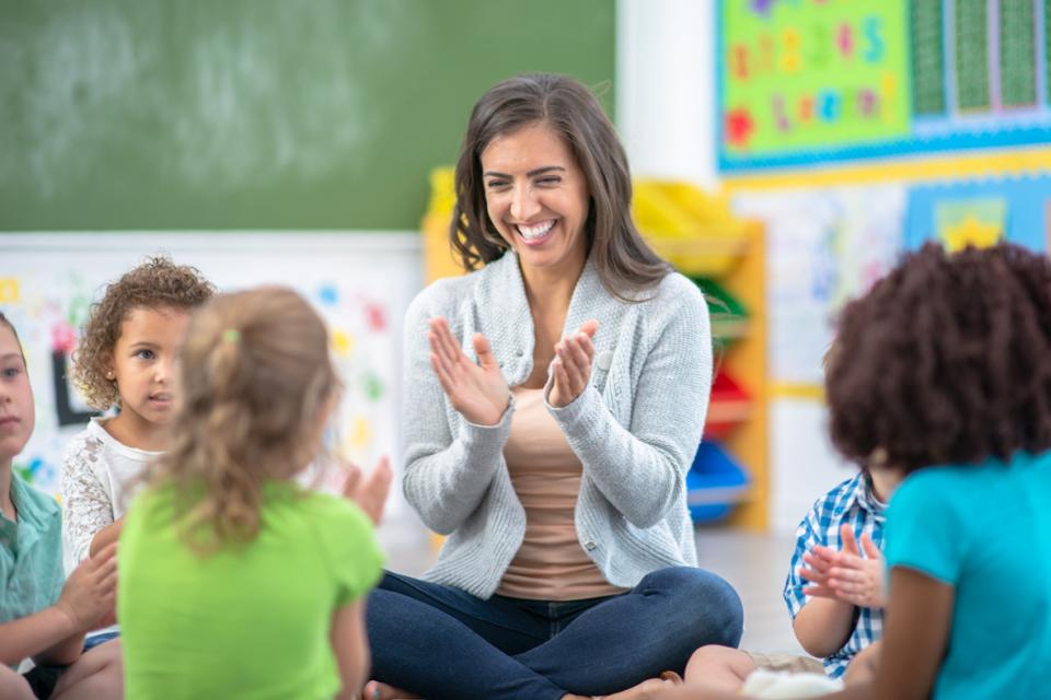 Enseignante assise sur le plancher avec les élèves et ils tapent des mains