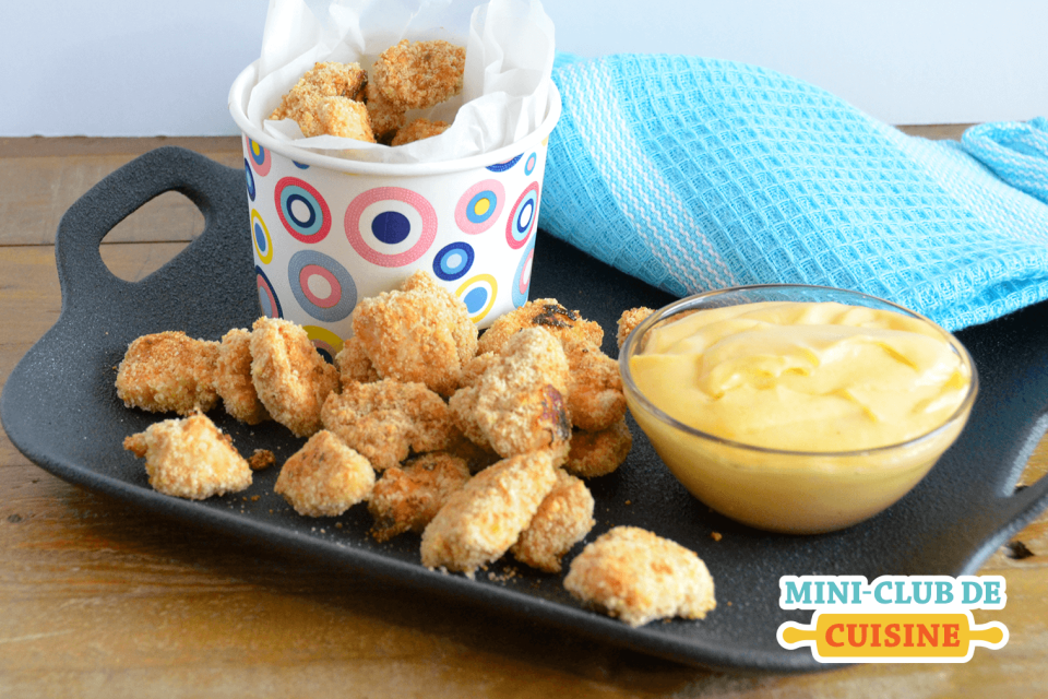 Poulet popcorn servi sur un plateau noir avec une sauce au fromage