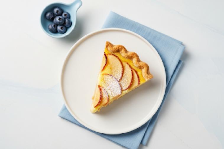 Image de haut en bas d'une tranche de tarte aux pommes et à la crème anglaise, garnie de sucre glace