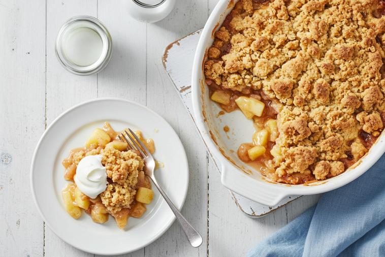 Crumble aux pommes et à la crème anglaise dans un plat avec une cocotte à côté