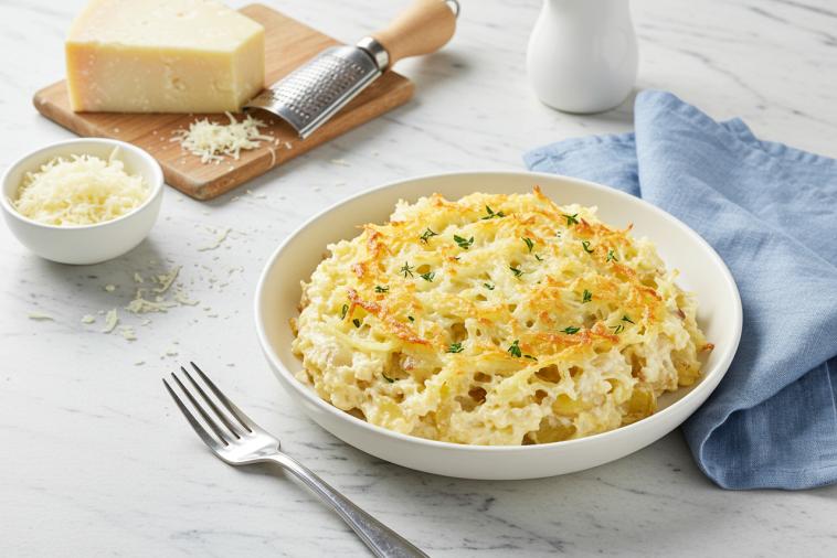 Casserole de pommes de terre râpées et de fromage dans un plat allant au four avec du parmesan en arrière-plan